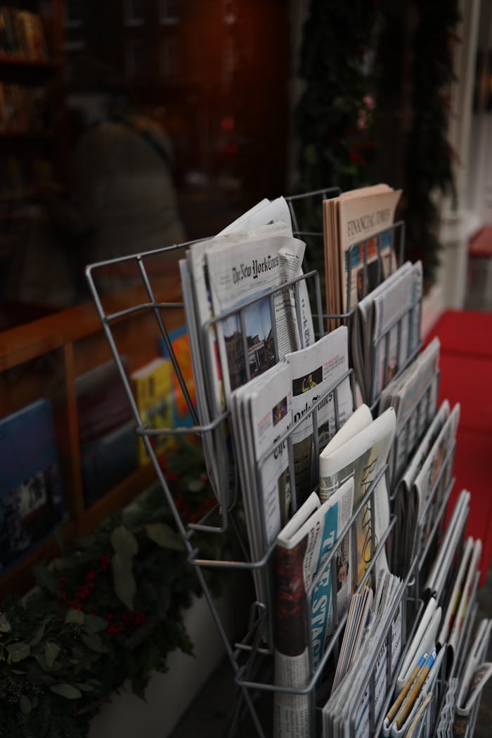 Street newsstand display featuring a range of newspapers and magazines in a cozy, urban setting.